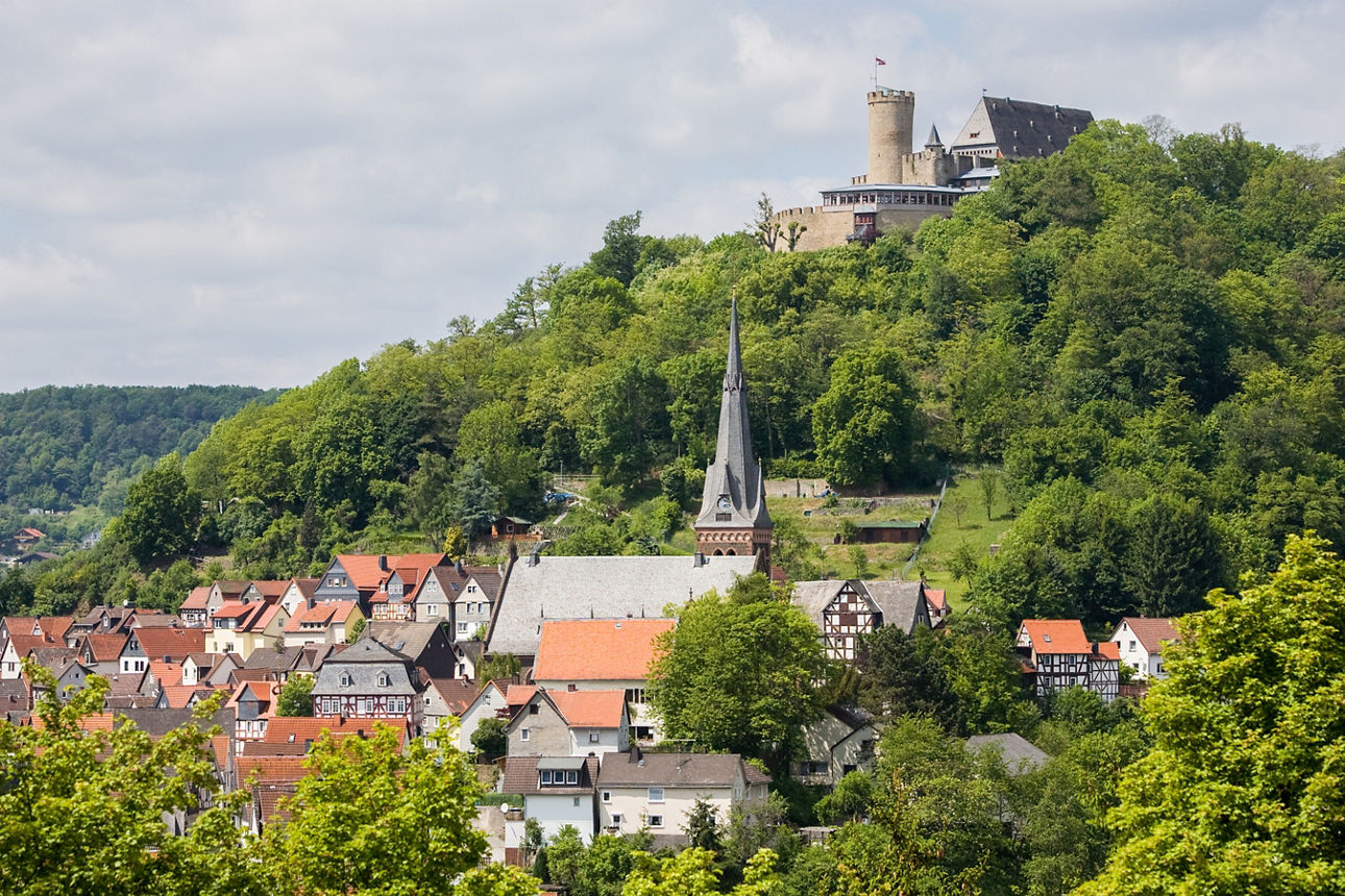 Blick auf die Stadt Biedenkopf mit ihren Fachwerkhäusern am Hang und dem Schloss Biedenkopf, das auf einem bewaldeten Hügel thront.