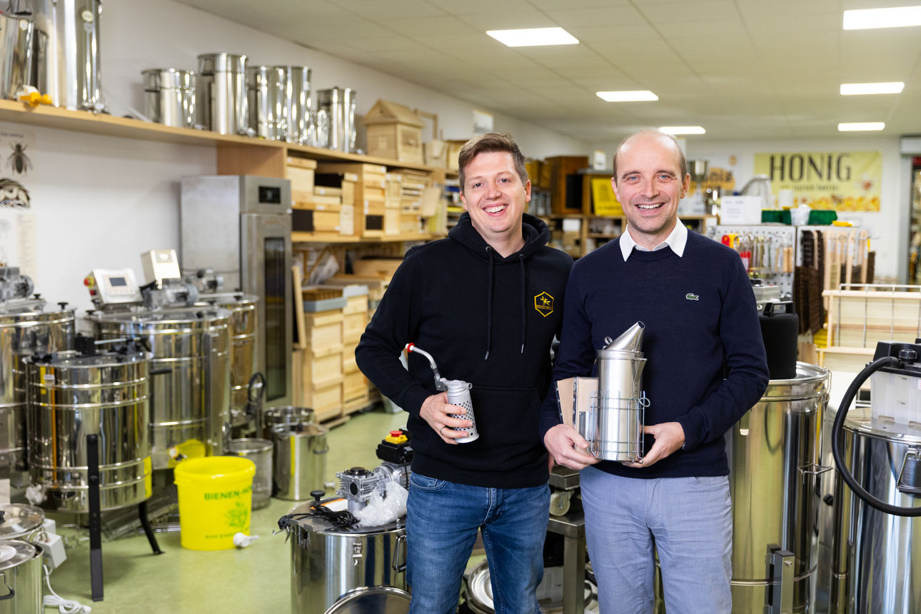 Inhaber Daniel Ruck und sein Bankberater Marco Müller in der Imkereiausstellung, umgeben von Geräten und Zubehör für die Honigverarbeitung.