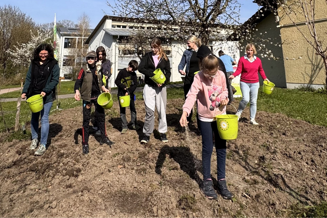 Auf dem Bild sind Schülerinnen und Schüler zu sehen die eine Wildblumenwiese ansäen