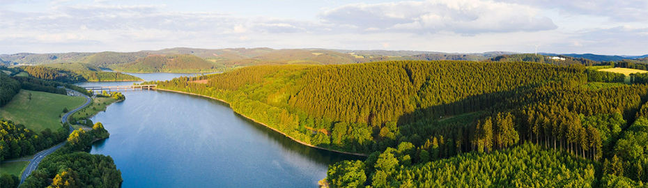 Der Biggesee im Sauerland liegt in einer grünen Landschaft mit vielen Hügeln umgeben von Hügeln.
