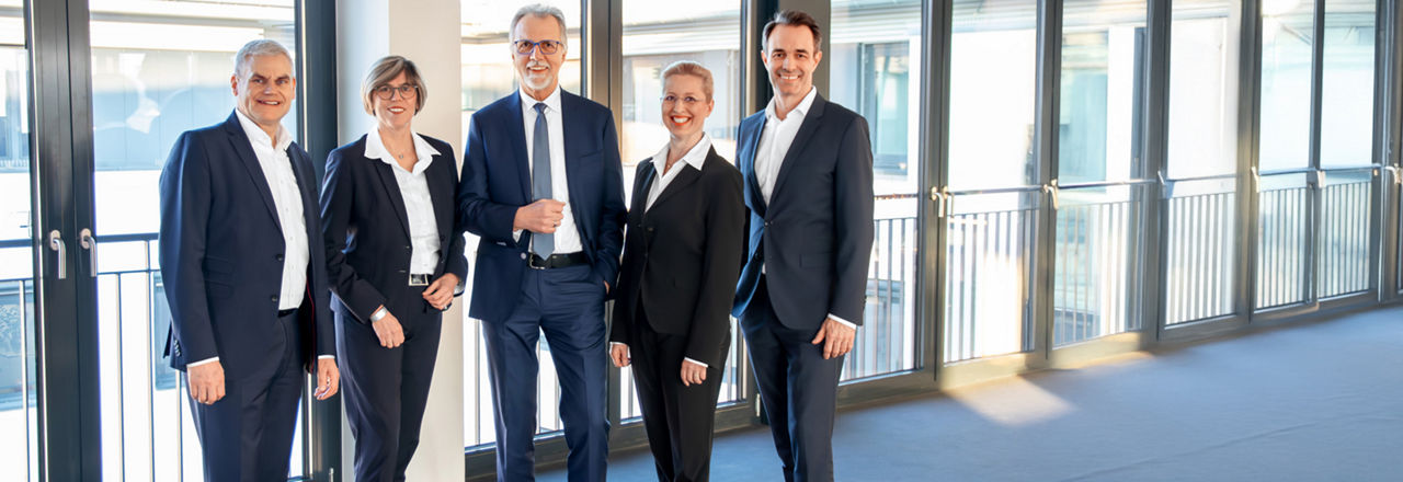 Das Bild zeigt eine Bilanzpressemitteilung. Drei Vorstände und zwei Aufsichtsräte stellen die Ergebnisse vor.