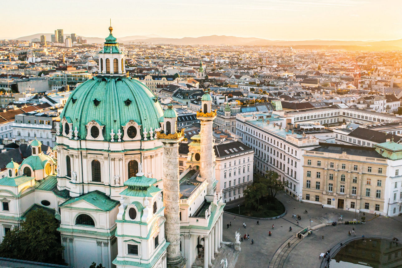 Luftaufnahme der barocken Karlskirche in Wien mit Kuppel und umliegender Stadt bei Sonnenuntergang