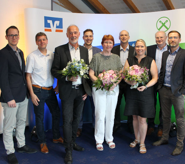 Eine bunt gemischte Gruppe von Menschen steht zusammen, jeder hält einen bunten Blumenstrauß und lächelt freundlich in die Ka