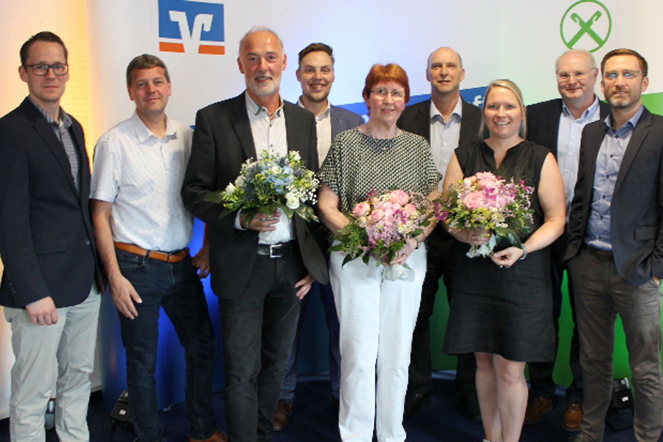 Eine bunt gemischte Gruppe von Menschen steht zusammen, jeder hält einen bunten Blumenstrauß und lächelt freundlich in die Ka