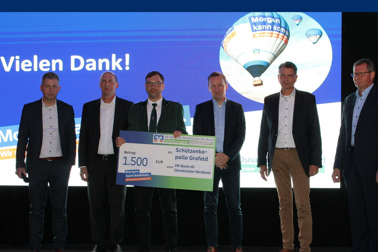 Eine Gruppe von Männern steht vor einem großen Bildschirm, auf dem ein Scheck angezeigt wird, und diskutiert oder feiert.