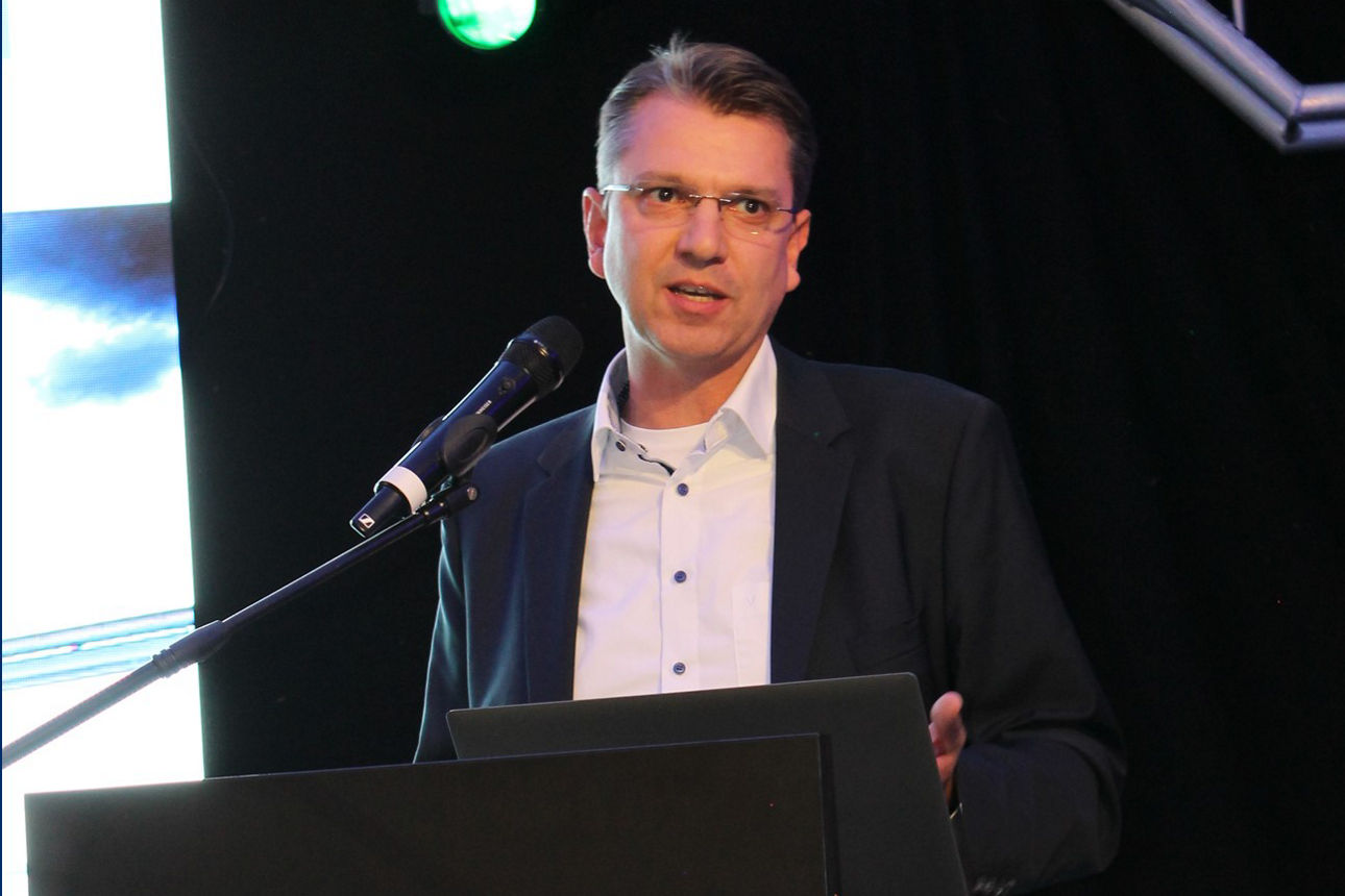 Ein Mann steht selbstbewusst auf einem Podium und hält eine Rede vor einem engagierten Publikum. 