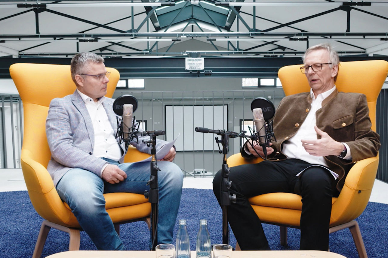 Zwei Personen im Gespräch vor Mikrofonen, Podcast- oder Interviewaufnahme in modernem Studio.