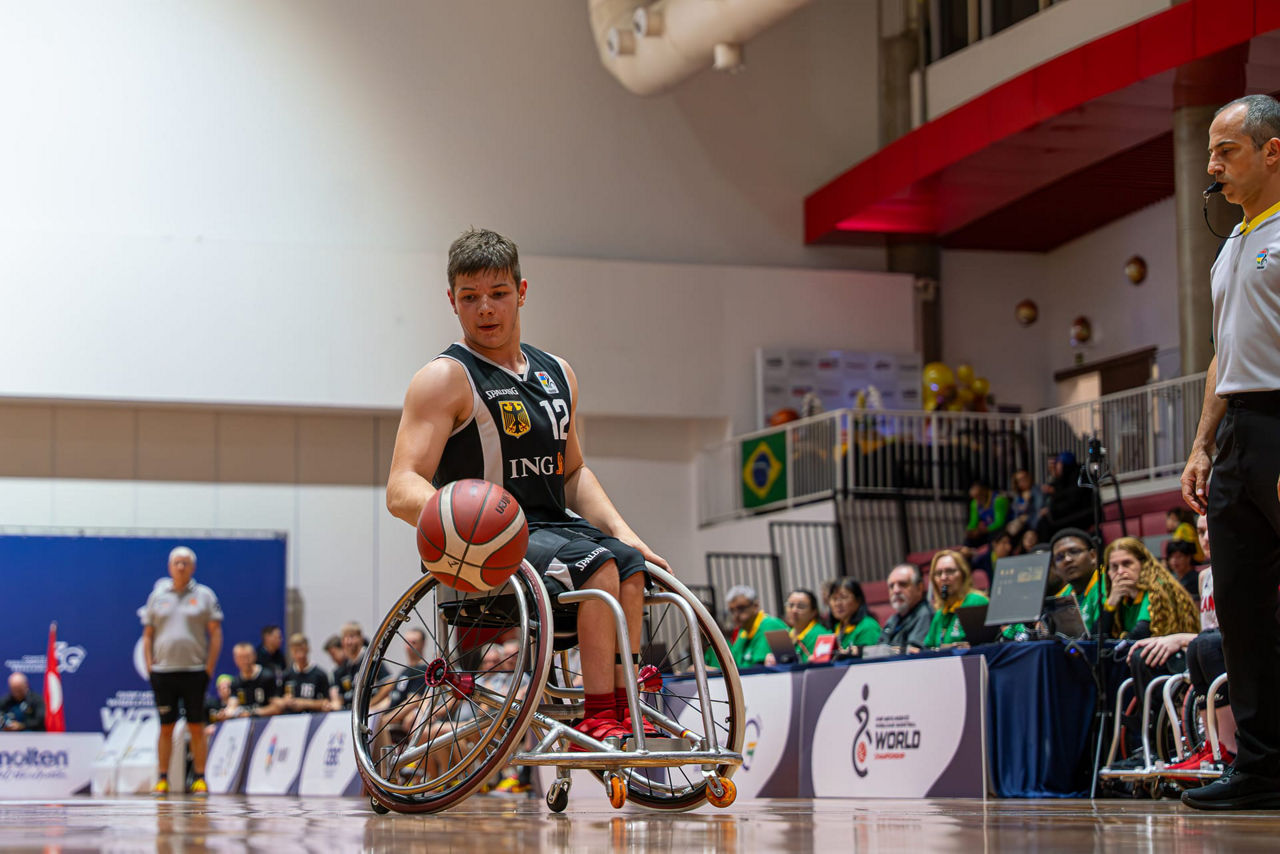 Ein Jugendlicher sitzt mit Trikot im Rollstuhl und spielt Rollstuhlbasketball