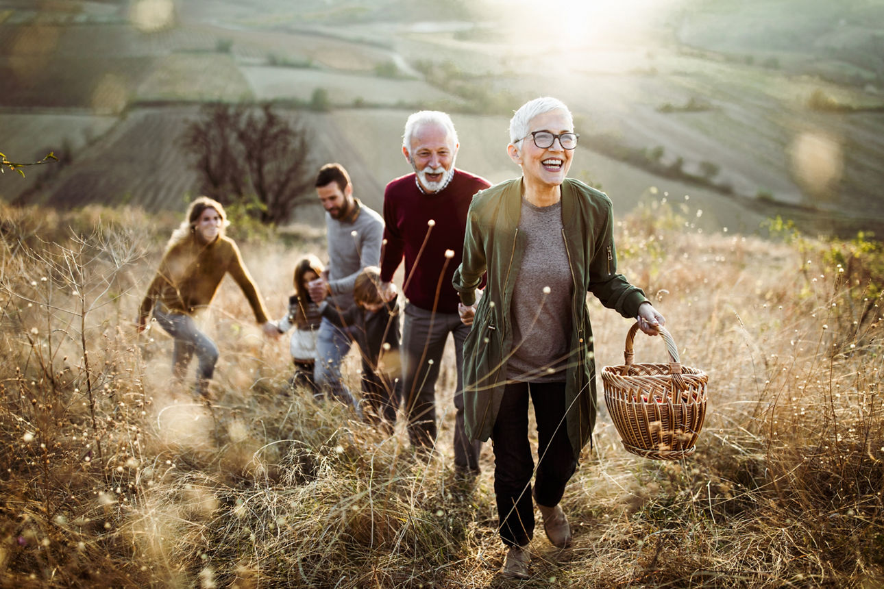 Happy mature woman holding hands with her family while moving up the hill towards their picnic place.