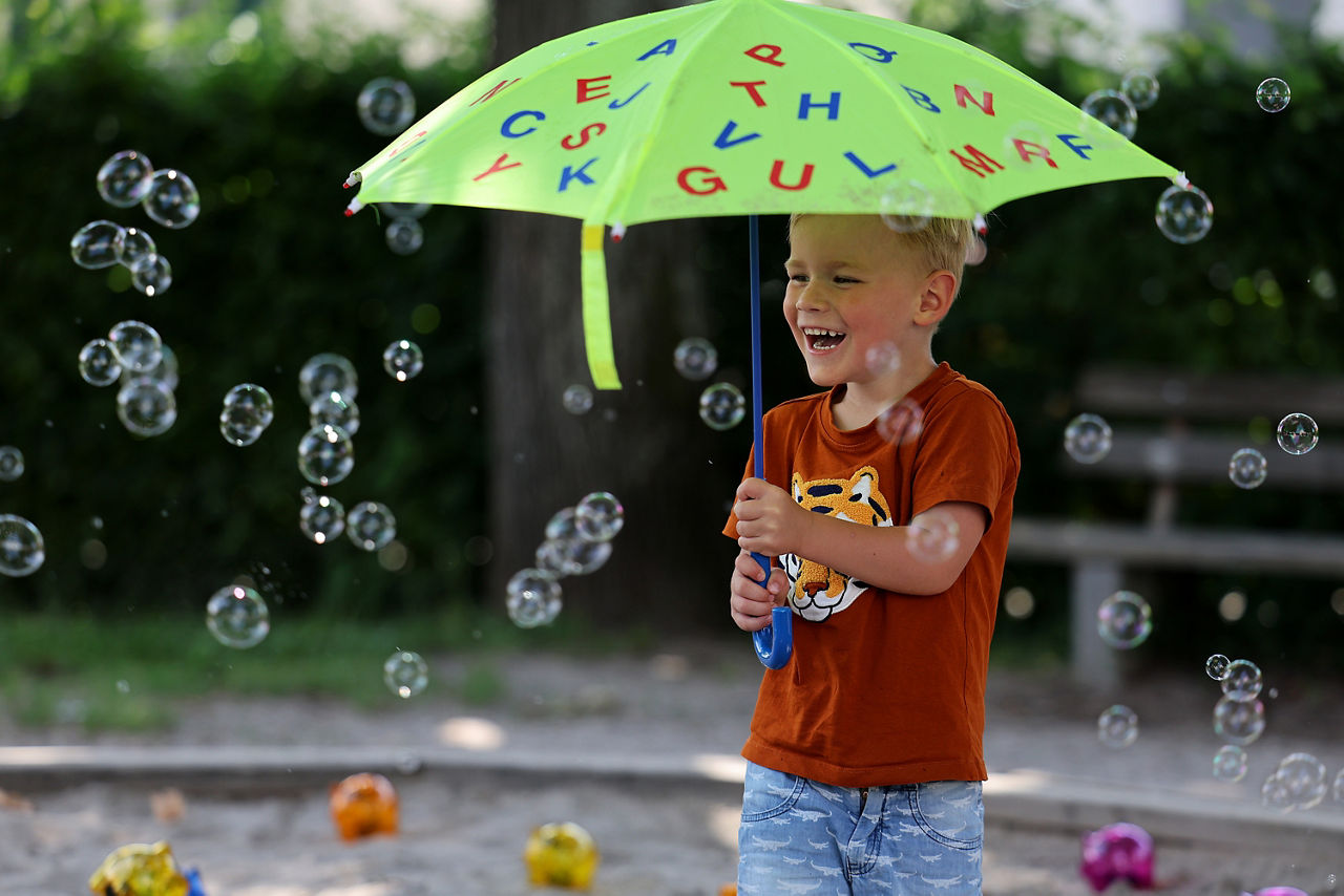 Bild eines kleinen lachenden Jungen mit einem grünen Regenschirm und Seifenblasen