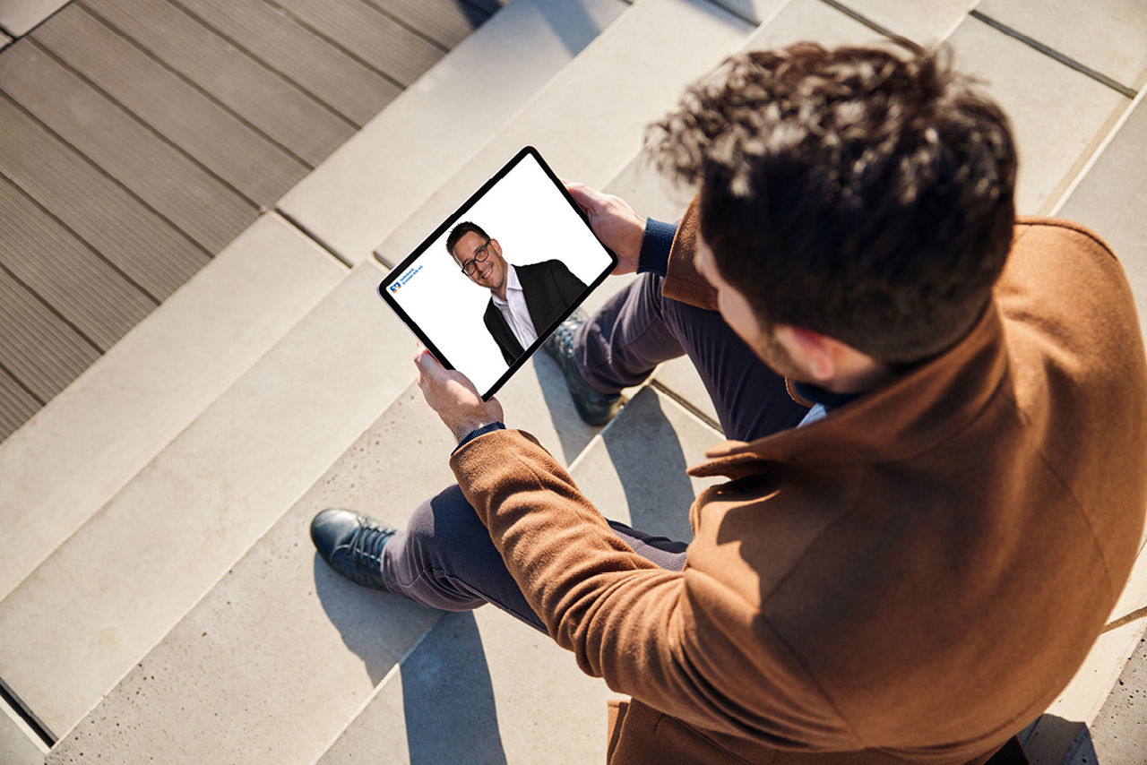 Mann sitzt mit einem Tablet in der Hand auf einer Treppe und macht die Digitalberatung