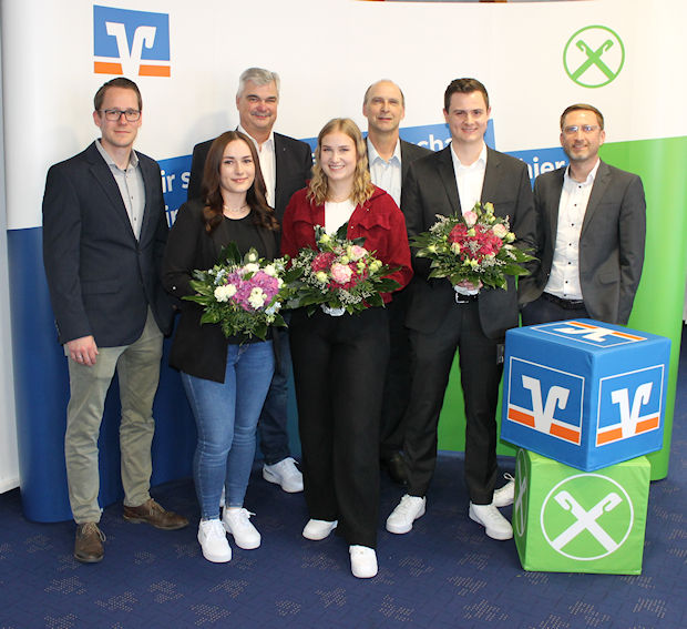 Eine bunt gemischte Gruppe von Menschen steht gemeinsam vor einem großen Banner, lächelt und unterhält sich miteinander.