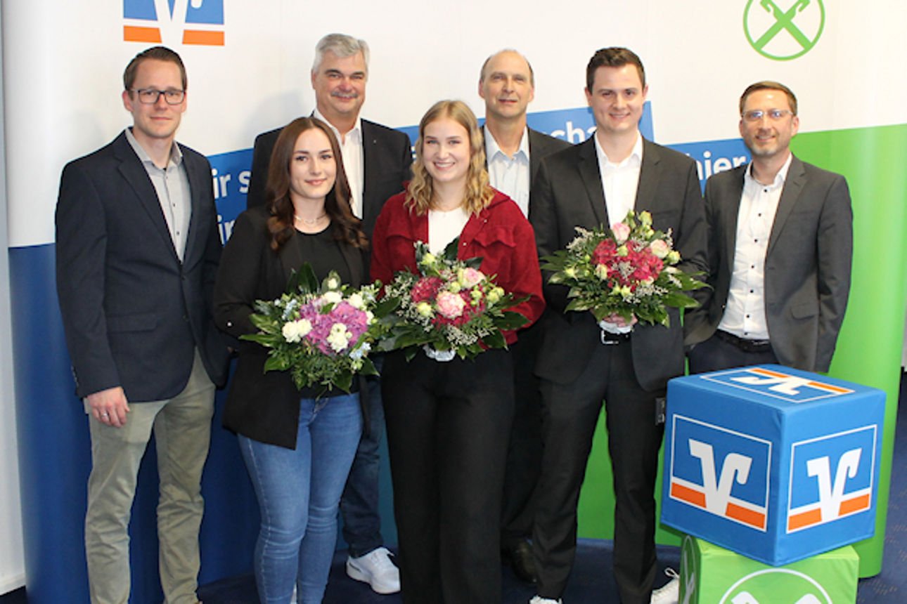 Eine bunt gemischte Gruppe von Menschen steht gemeinsam vor einem großen Banner, lächelt und unterhält sich miteinander.
