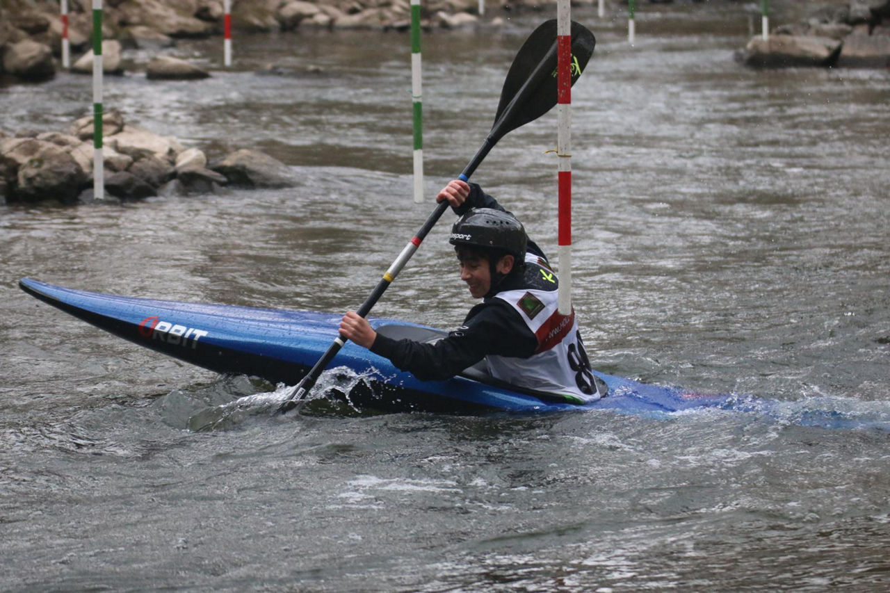 Kanusportler steuert ein Kajak durch einen Wildwasser-Parcours und passiert dabei Torstangen auf einer Slalomstrecke.