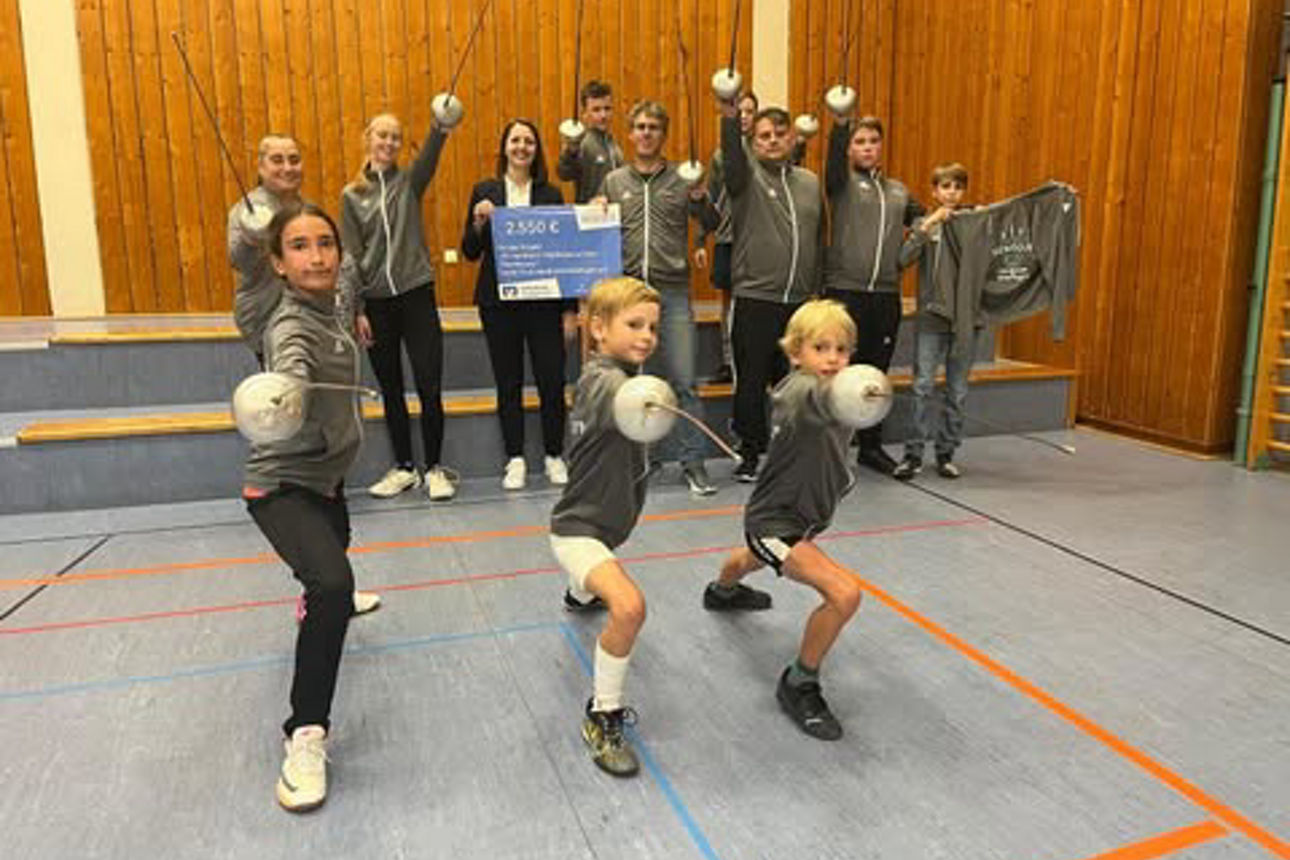 Fechterinnen und Fechter präsentieren sich mit Degen in Fechtstellung, im Hintergrund weitere Vereinsmitglieder mit einem Spe