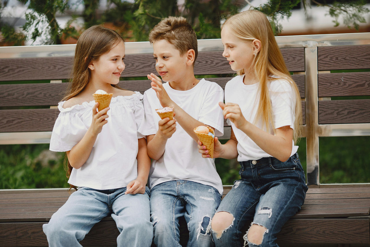 Drei Kinder sitzen auf einer Bank und essen Eis