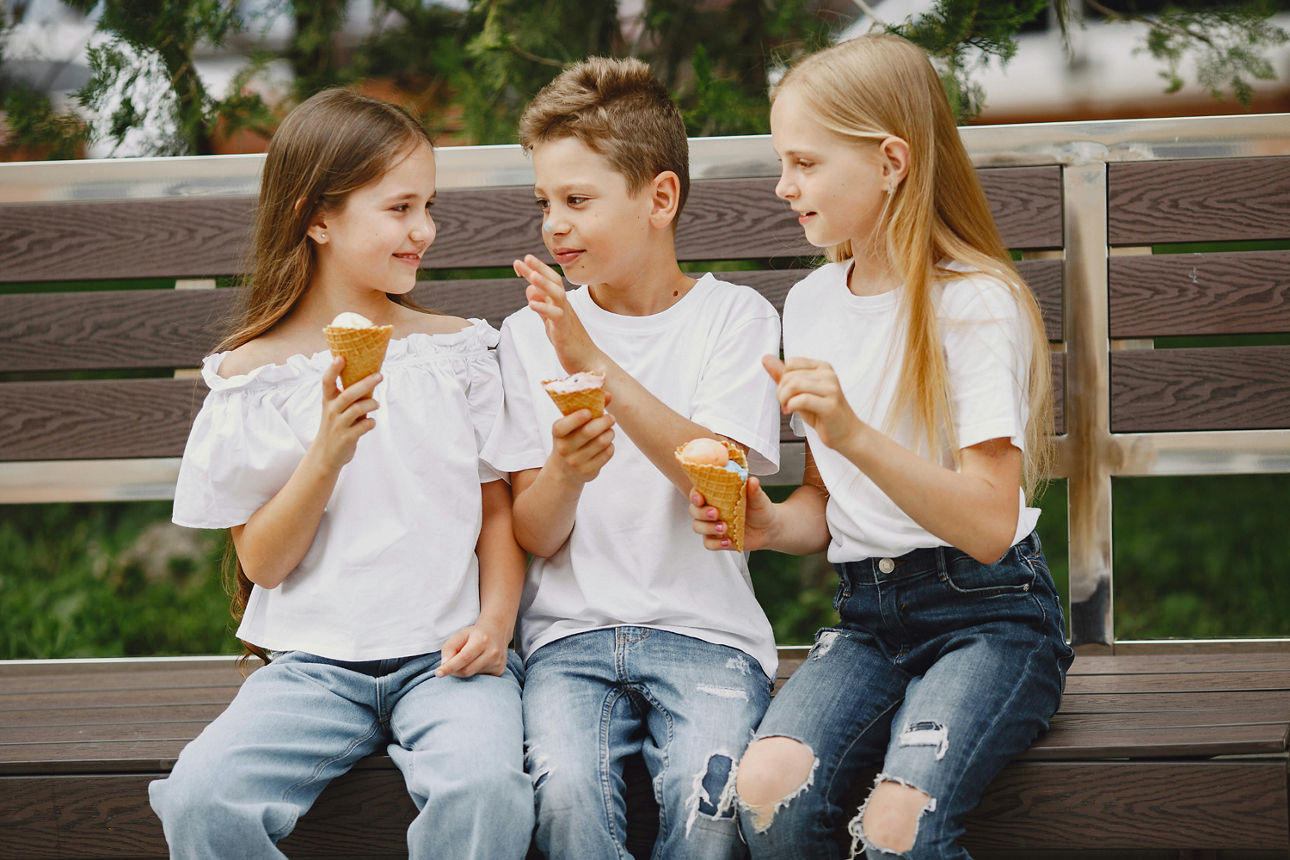 Drei Kinder sitzen auf einer Bank und essen Eis