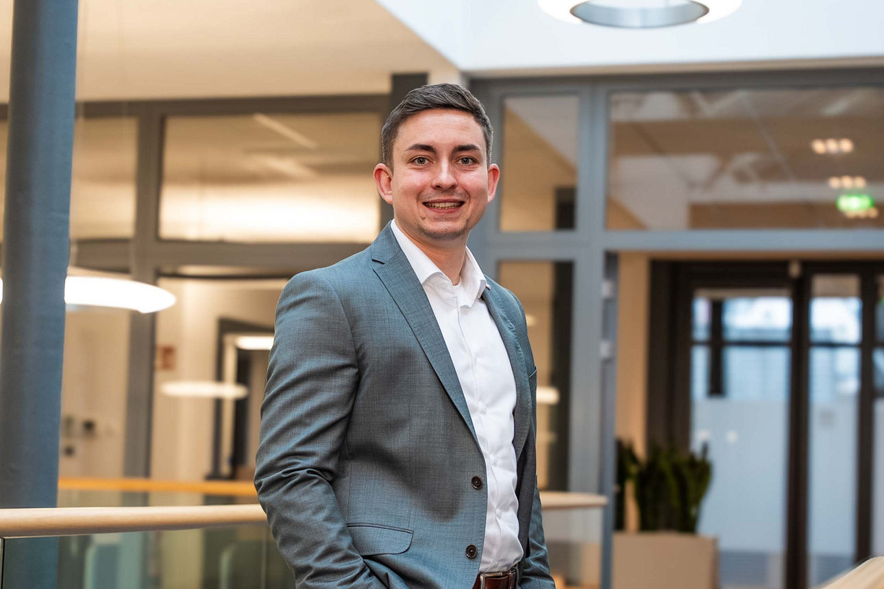 Ein Mann steht lächelnd in hellen Büroräumen