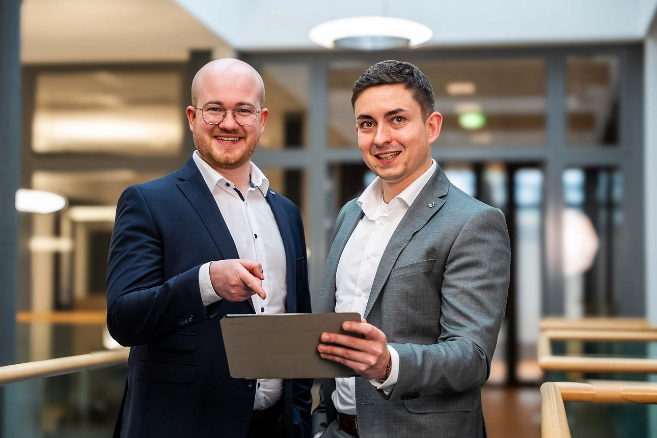 Zwei lächelnde Männer zeigen auf ein Laptop