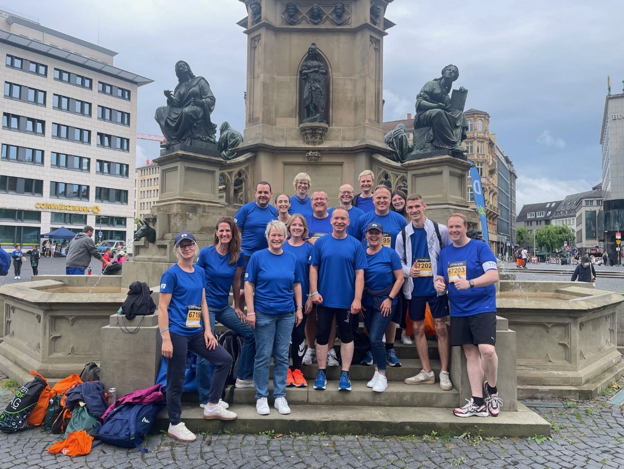 Mitarbeiter der Bank stehen mit blauem Trikot vor einem Brunnen in Frankfurt.