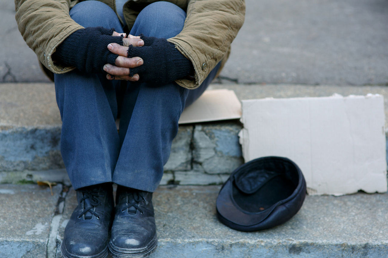 Ein Wohnungsloser sitzt auf einer Bordsteinkante und hält sich die Knie zusammen