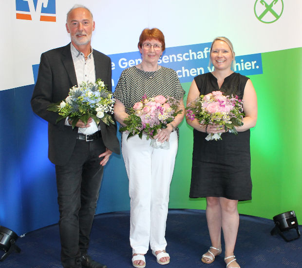 Eine bunt gemischte Gruppe von Menschen steht zusammen, jeder hält einen bunten Blumenstrauß und lächelt freundlich in die Ka