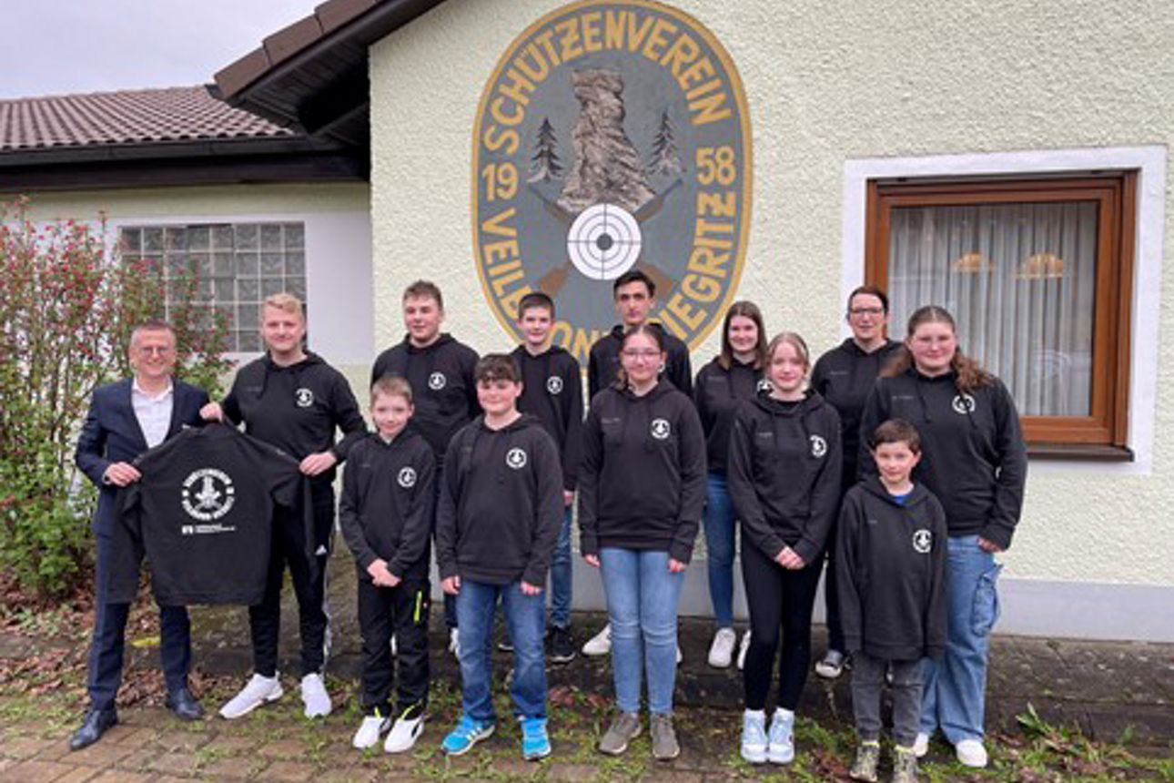 Eine Gruppe junger Schützen und ihre Mentoren posieren stolz vor einem Schießstand