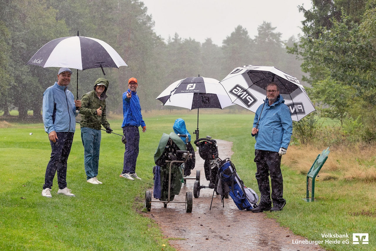 Vier Golfspieler auf dem Golfplatz mit ihren Golf-Caddys unter großen Regenschirmen, es regnet stark