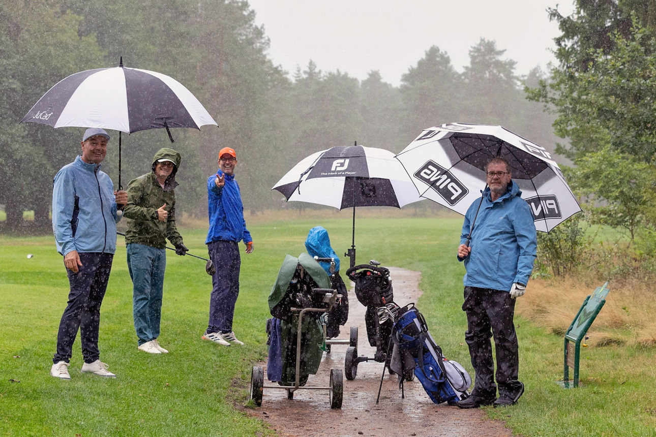 vier Golfer auf dem Golfplatz, es regnet in Strömen, sie haben Regenschirme
