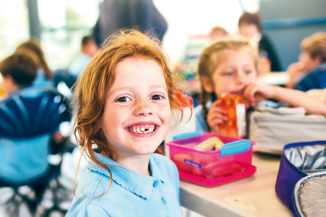 Erstklässlerin sitzt im Klassenzimmer und lacht
