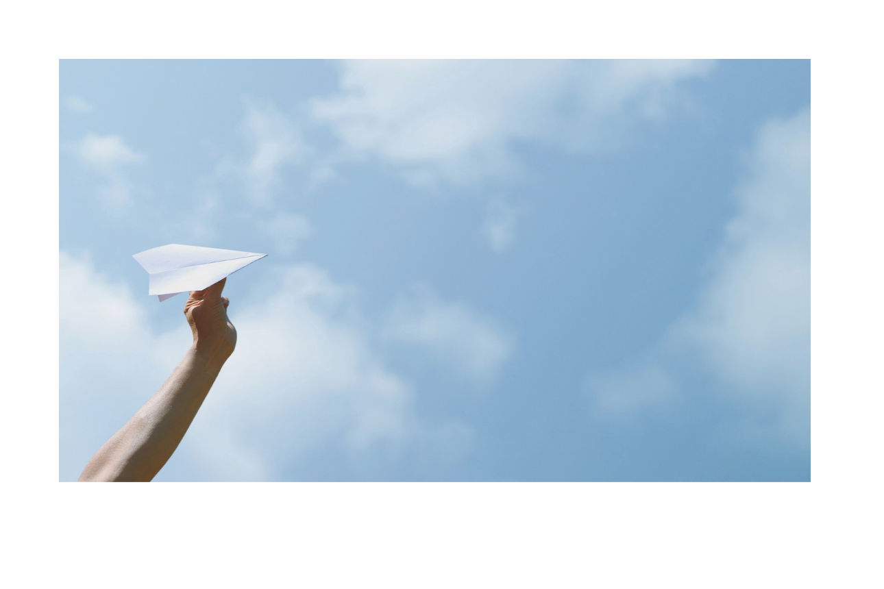 Eine Hand hält einen Papierflieger vor einem blauen Himmel mit leichten Wolken in die Höhe.