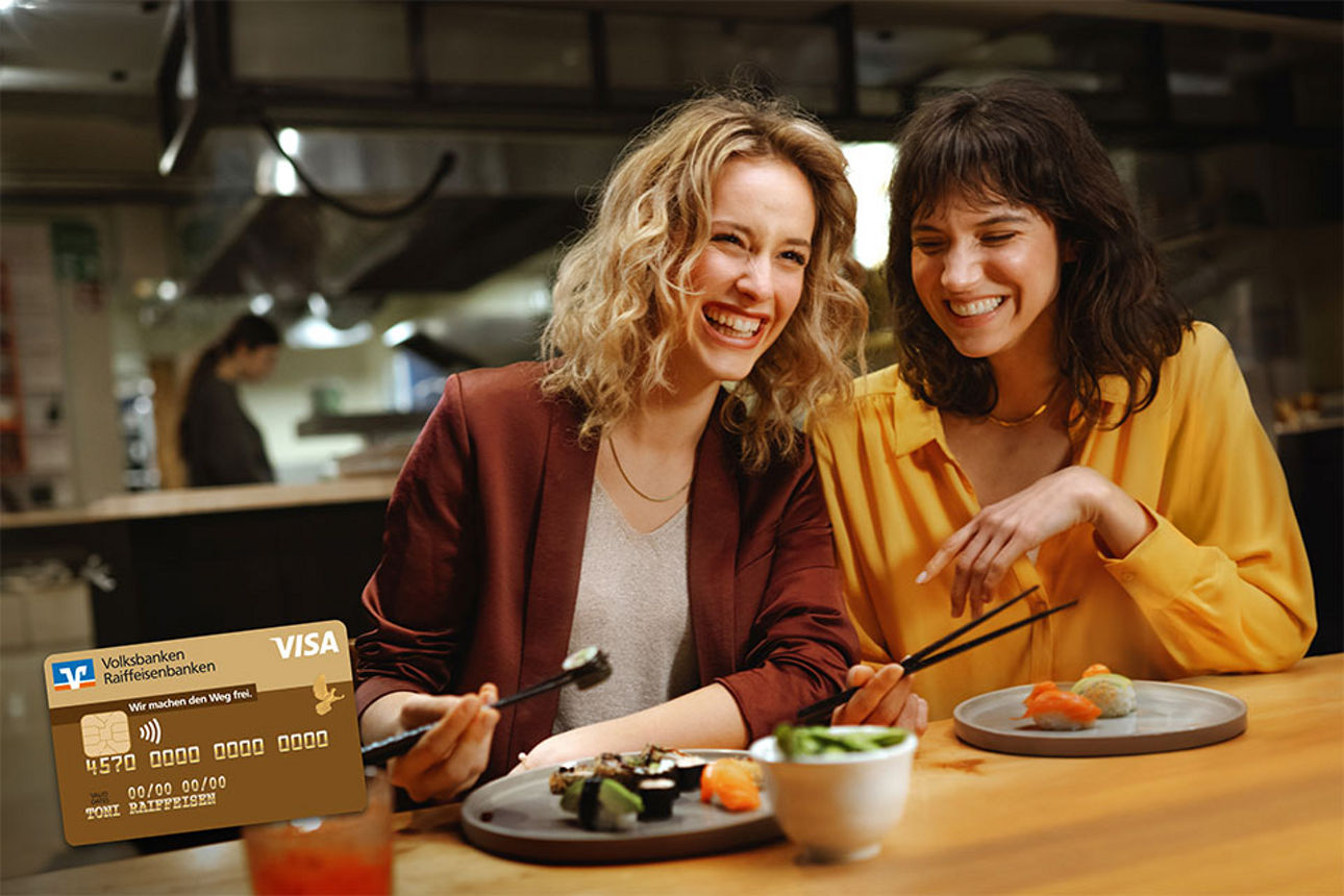 Zwei Frauen im Restaurant lächeln - eine Visa GoldCard link im Bild