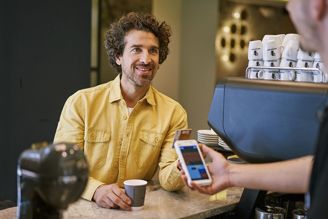 Ein lächelnder junger Mann bezhalt in einer Kaffeebar seinen Kaffee mit einer Girocard