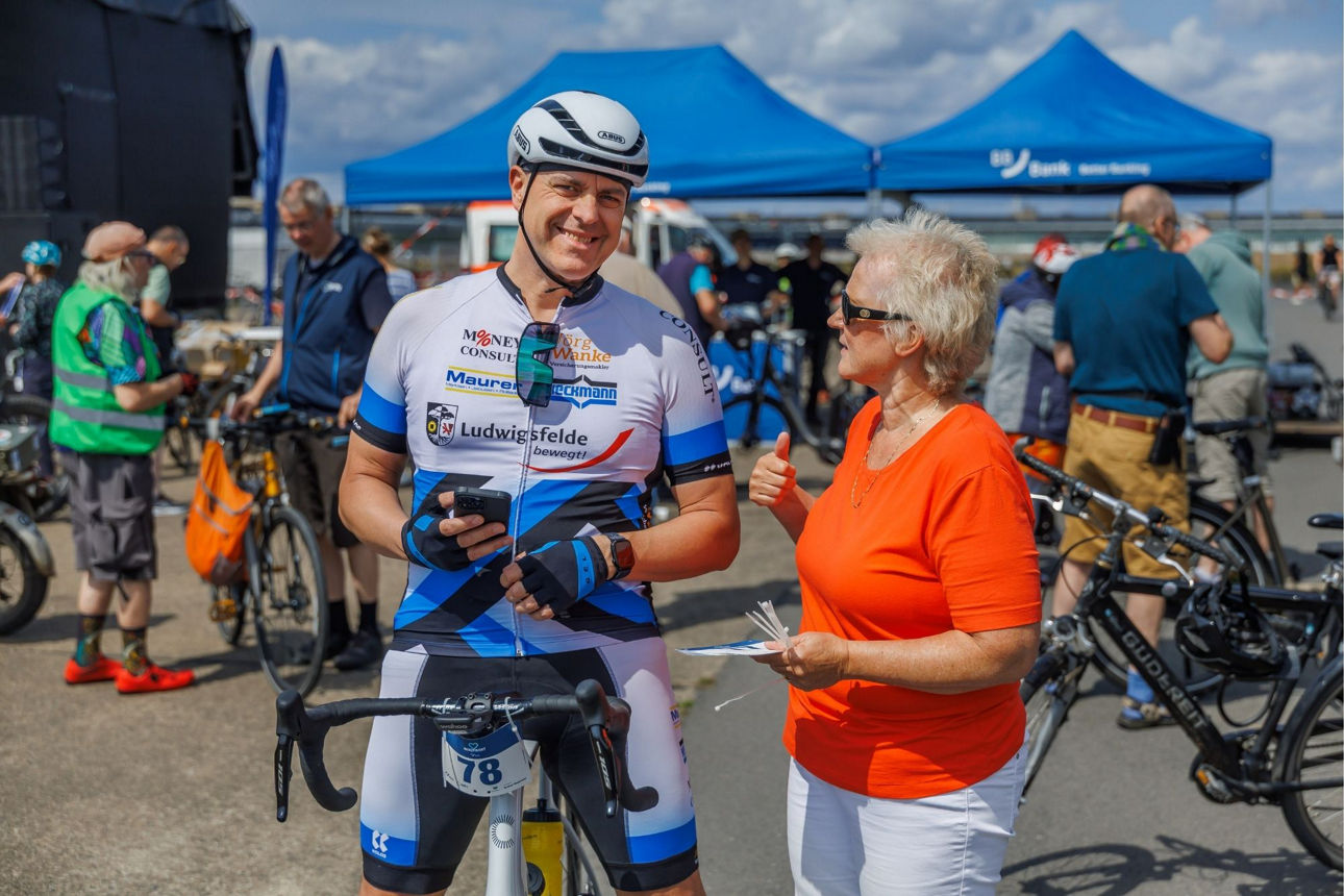 Radfahrer schaut in die Kamera während im eine Frau etwas erklärt