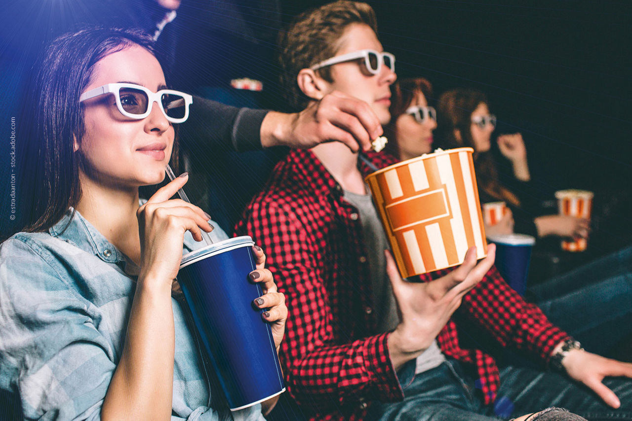Zwei Personen sitzen mit Getränk und Popcorn im Kino