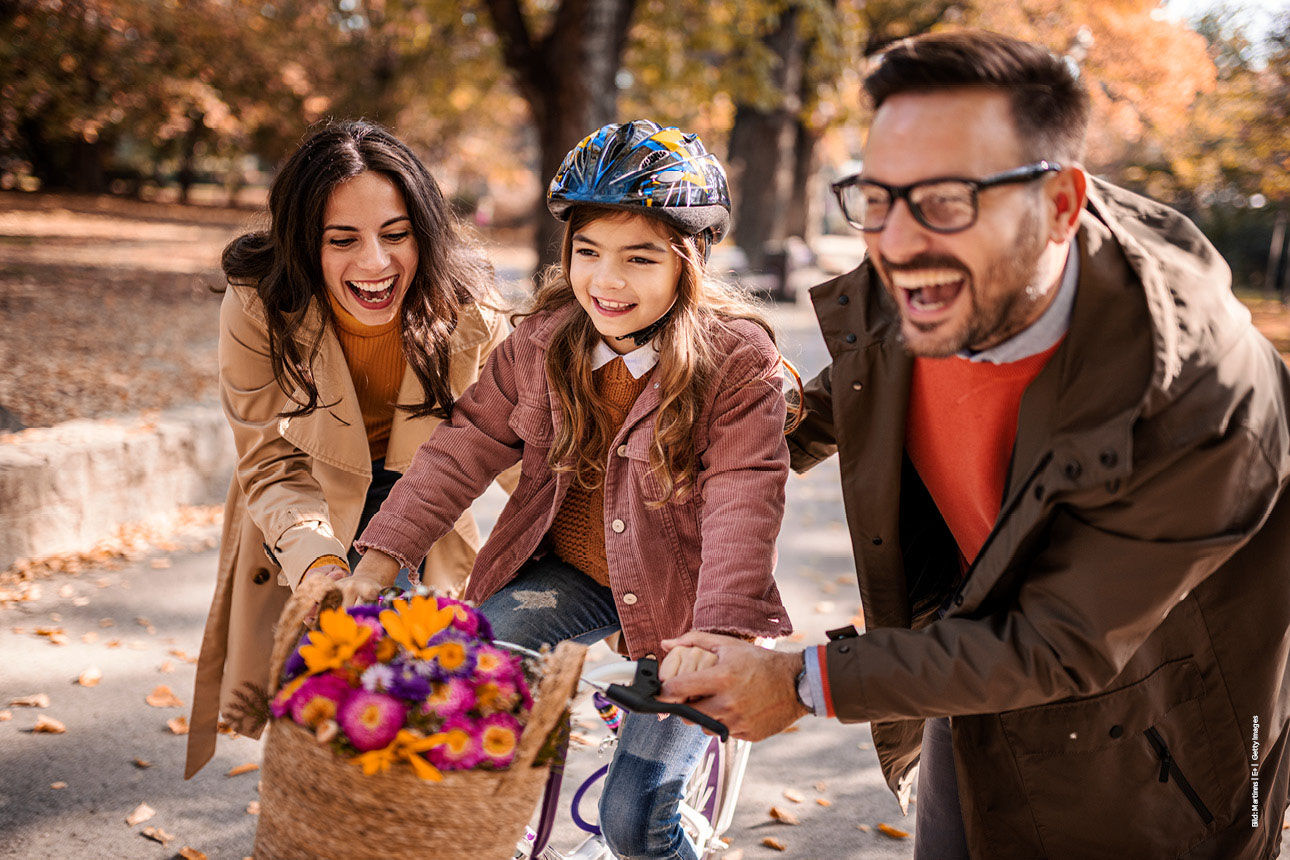 Mutter und Vater helfen dem Mädchen beim Fahrradfahren und lachen dabei