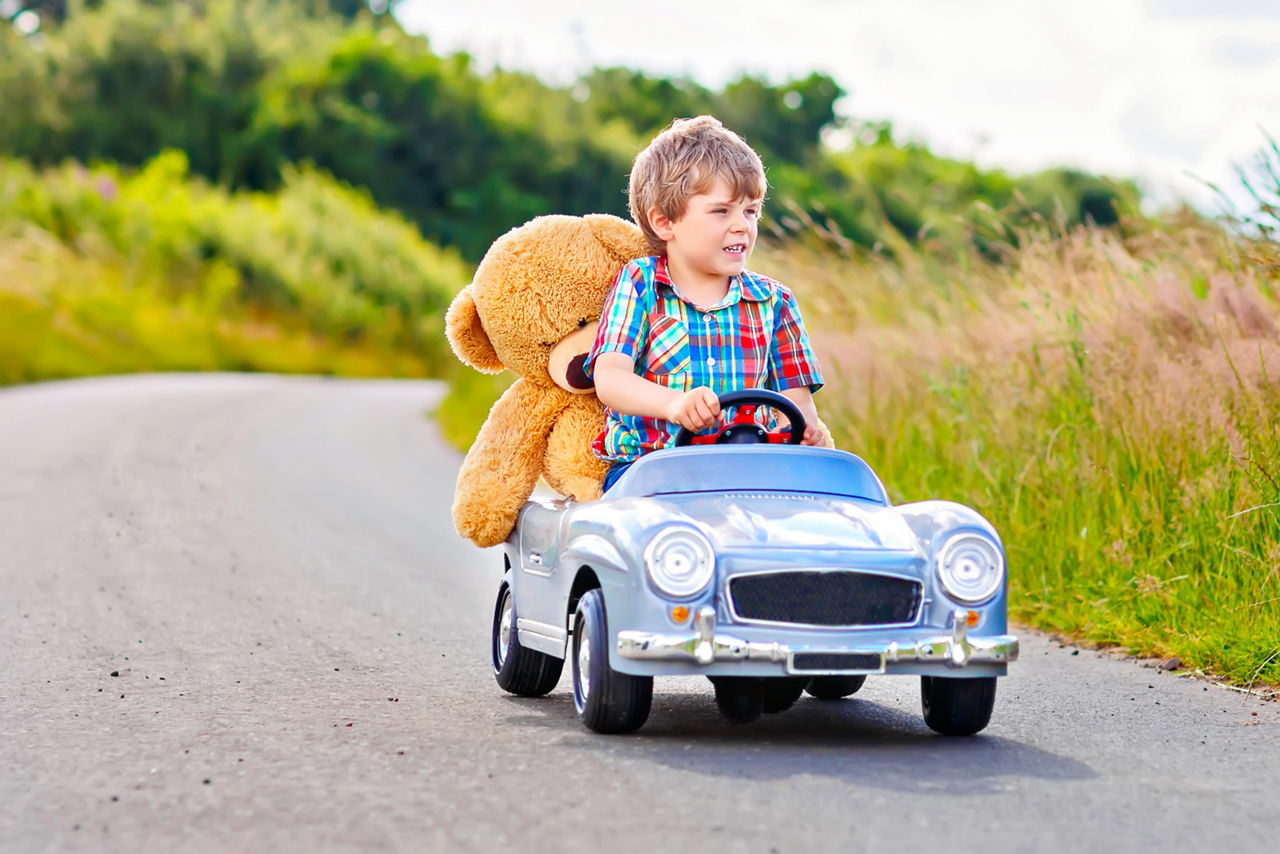 Kleiner Junge im Kinder-Auto mit Teddy an Board