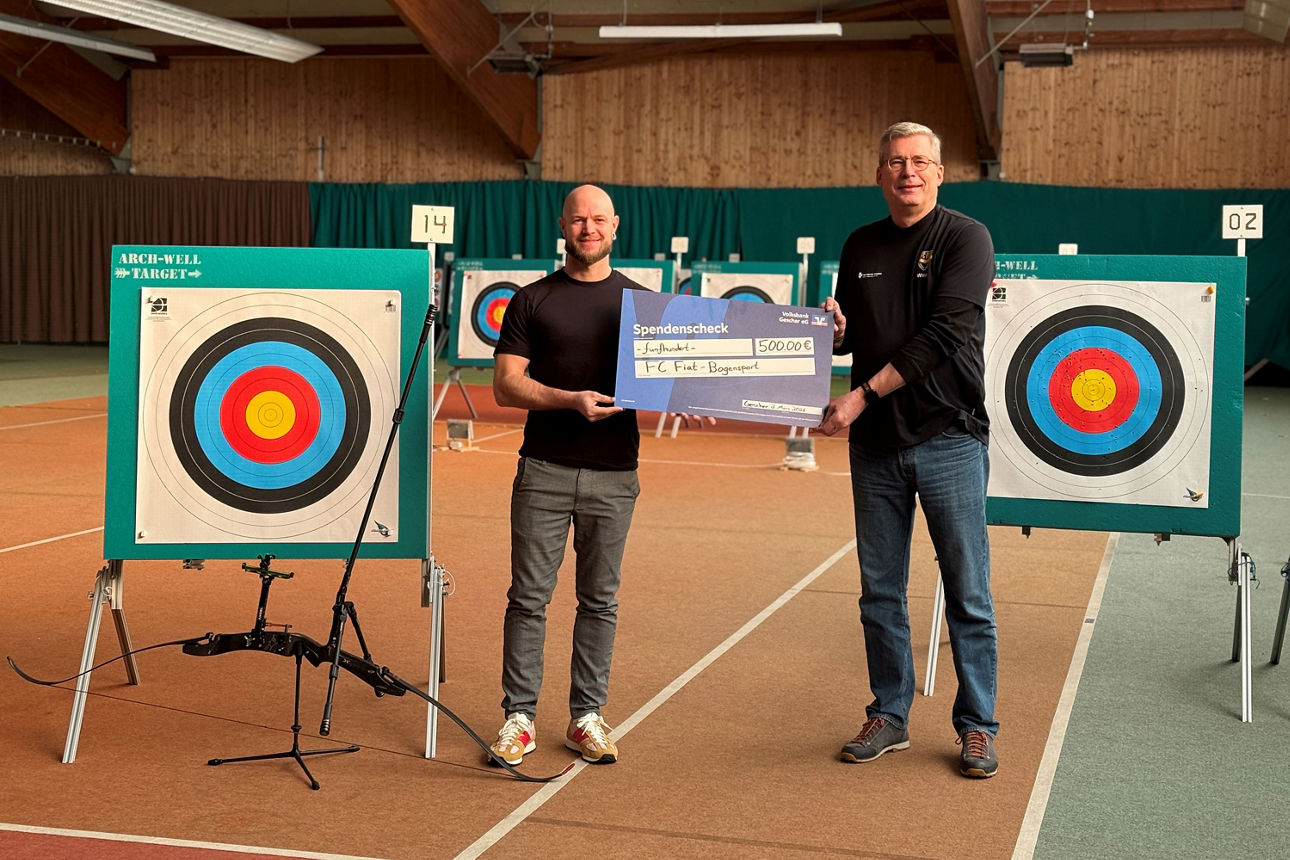 zwei Männer halten einen symbolischen Scheck in den Händen, während sie neben zwei Zielscheiben für Bogenschießen stehen