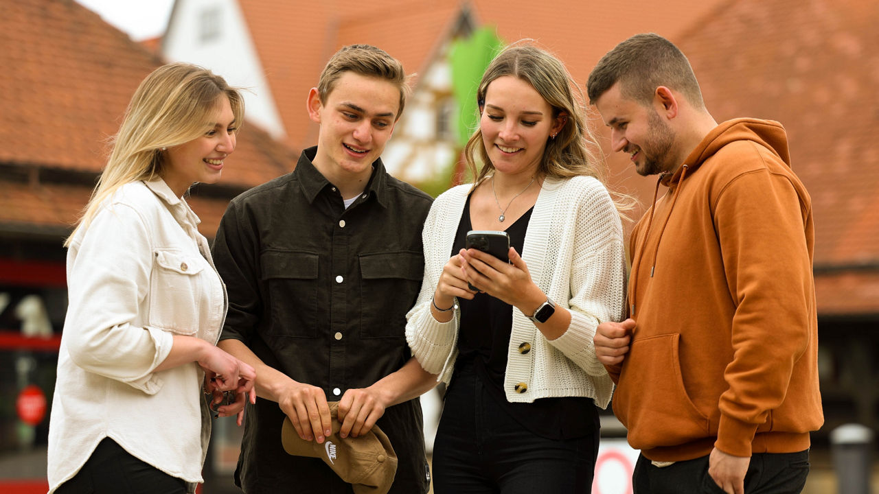 Eine Gruppe von 4 jungen Leuten stehen zusammen und schauen gemeinsam auf ein Handy