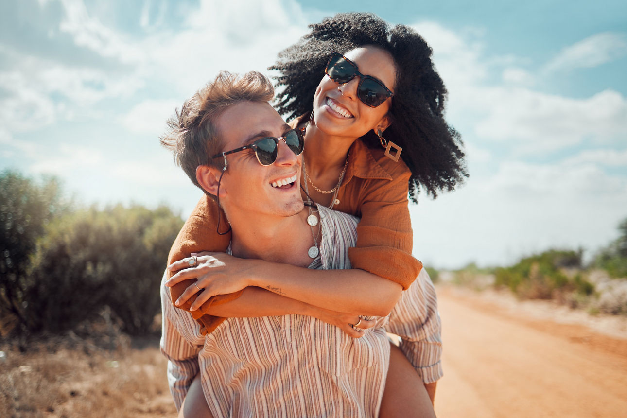 Love, happy and couple piggy back on road path in Arizona desert in USA for romantic getaway. Interracial people dating smile while enjoying summer romance on travel holiday adventure together.