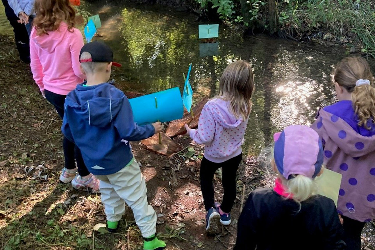 Kinder beobachten selbstgebaute Boote im Fluss