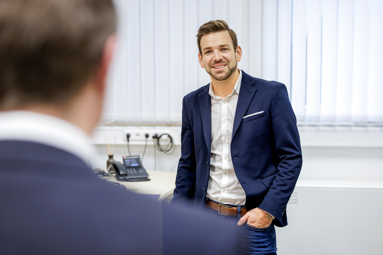 Ein Berater steht im Büro und bergrüßt einen Kunden.