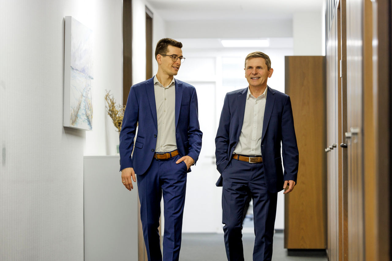 Zwei Bankvorstände laufen gemeinsam den Flur der Bank entlang und schauen sich an.