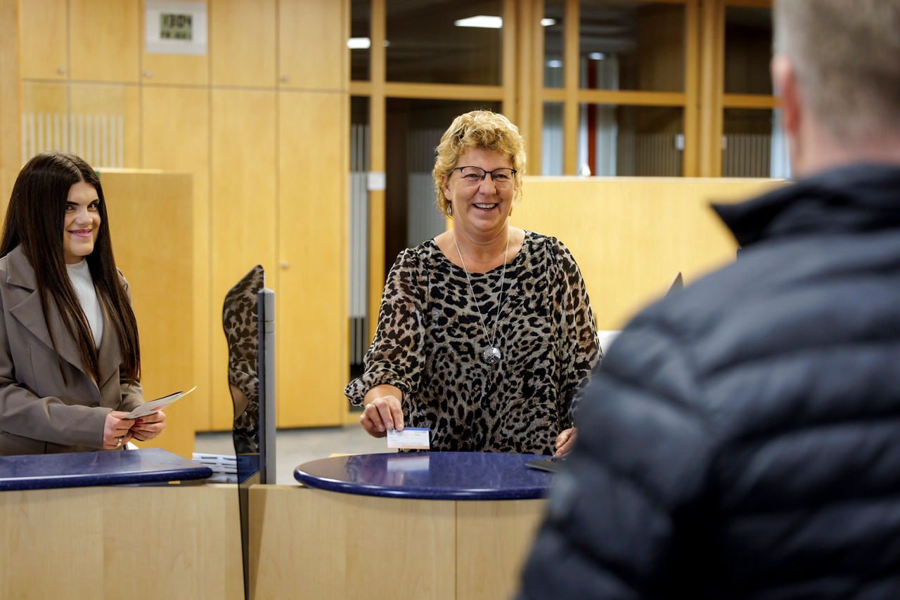 Zwei Mitarbeiterinnen stehen hinter dem Kundenschalter und bedienen einen Kunden.