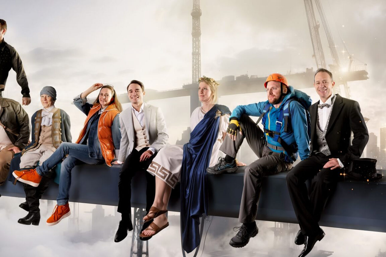 Mitarbeitende sitzen auf Stange mit Skyline im Hintergrund