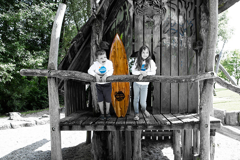 Kinder stehen zusammen mit einem Surfbrett am Spielplatz.