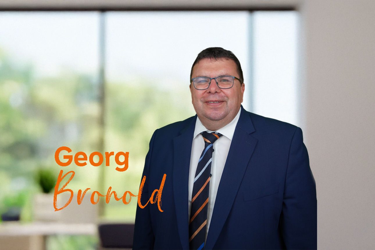 Das Bild zeigt einen Mann in einem Büro mit einem orangen Text "Georg Bronold"