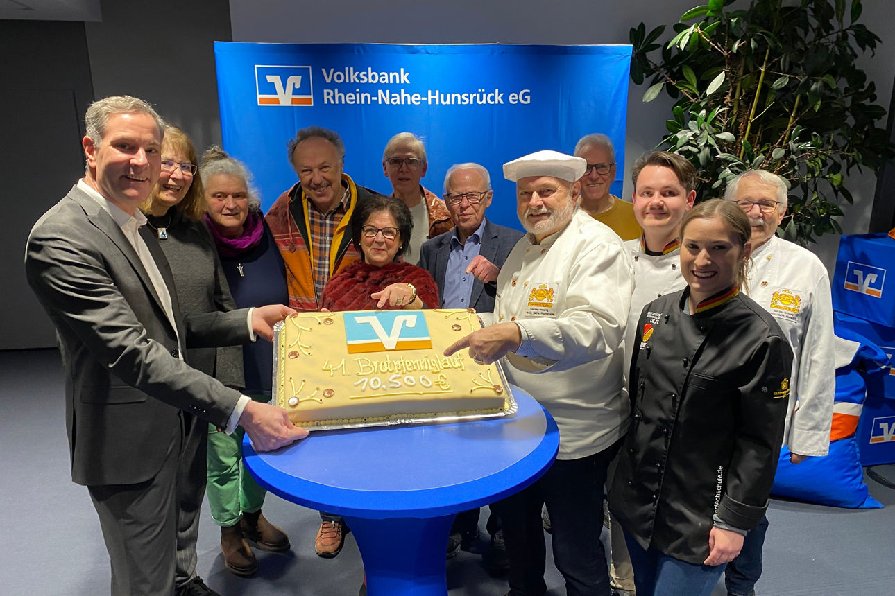 Eine Gruppe von Erwachsenen stehen vor einem Stehtisch und präsentieren die Brotpfennig Torte.