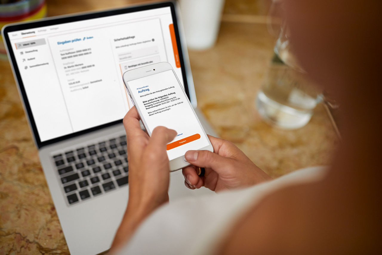 Frau hält Handy in der Hand und davor ist ein Laptop