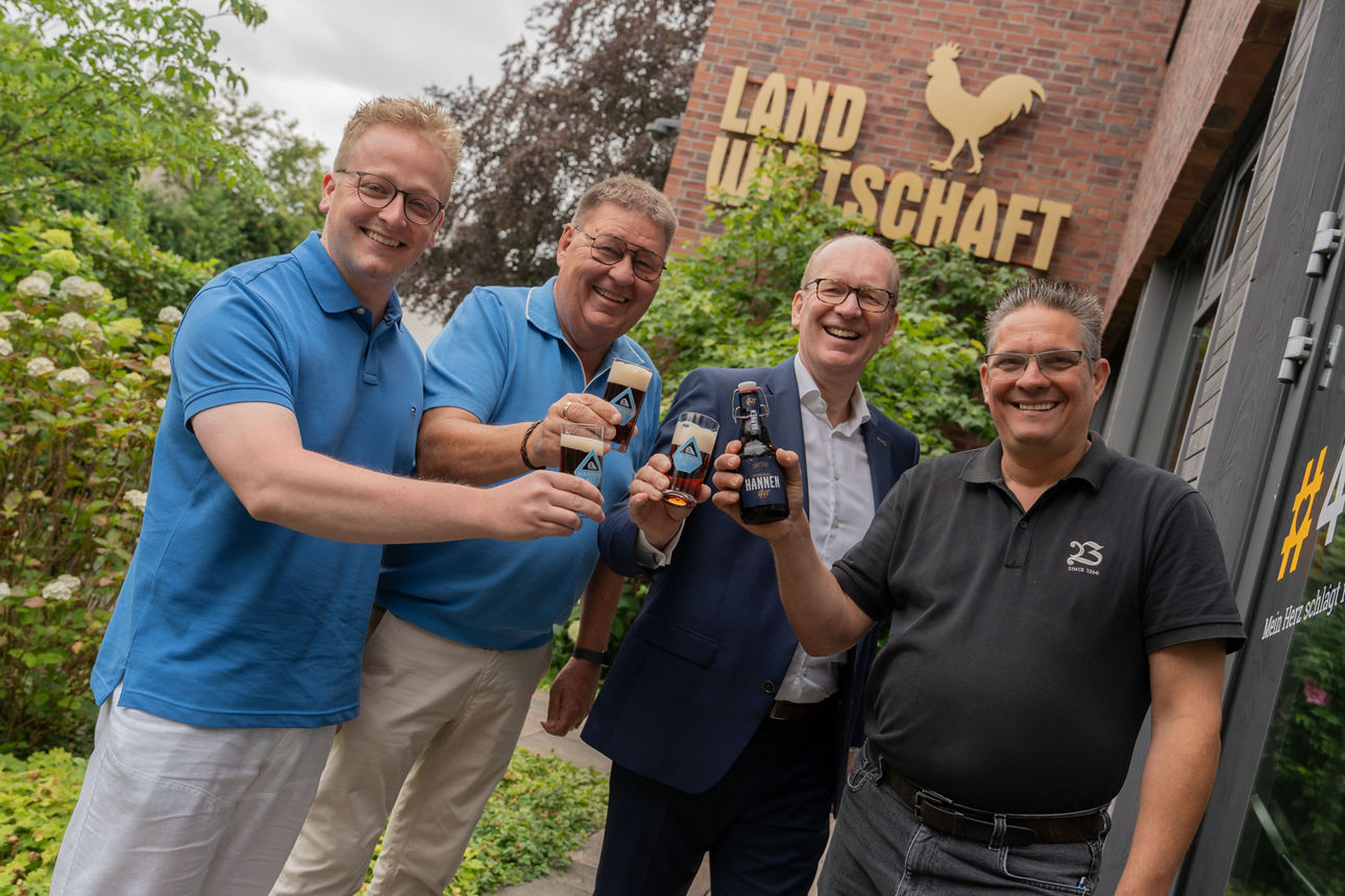 Vier Männer stehen vor dem Gebäude der Brauerei Bolten und halten lächelnd gefüllte Biergläser beziehungsweise eine Bierflasc